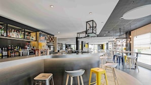 A modern bar area with stools, shelves of bottles, and a bar counter. - Campanile Roissy - Aéroport CDG - Le Mesnil Amelot (Le Mesnil-Amelot)