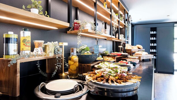 A buffet setup with various dishes, a sink, and shelves with items like bottles and plants. - Campanile Roissy - Aéroport CDG - Le Mesnil Amelot (Le Mesnil-Amelot)