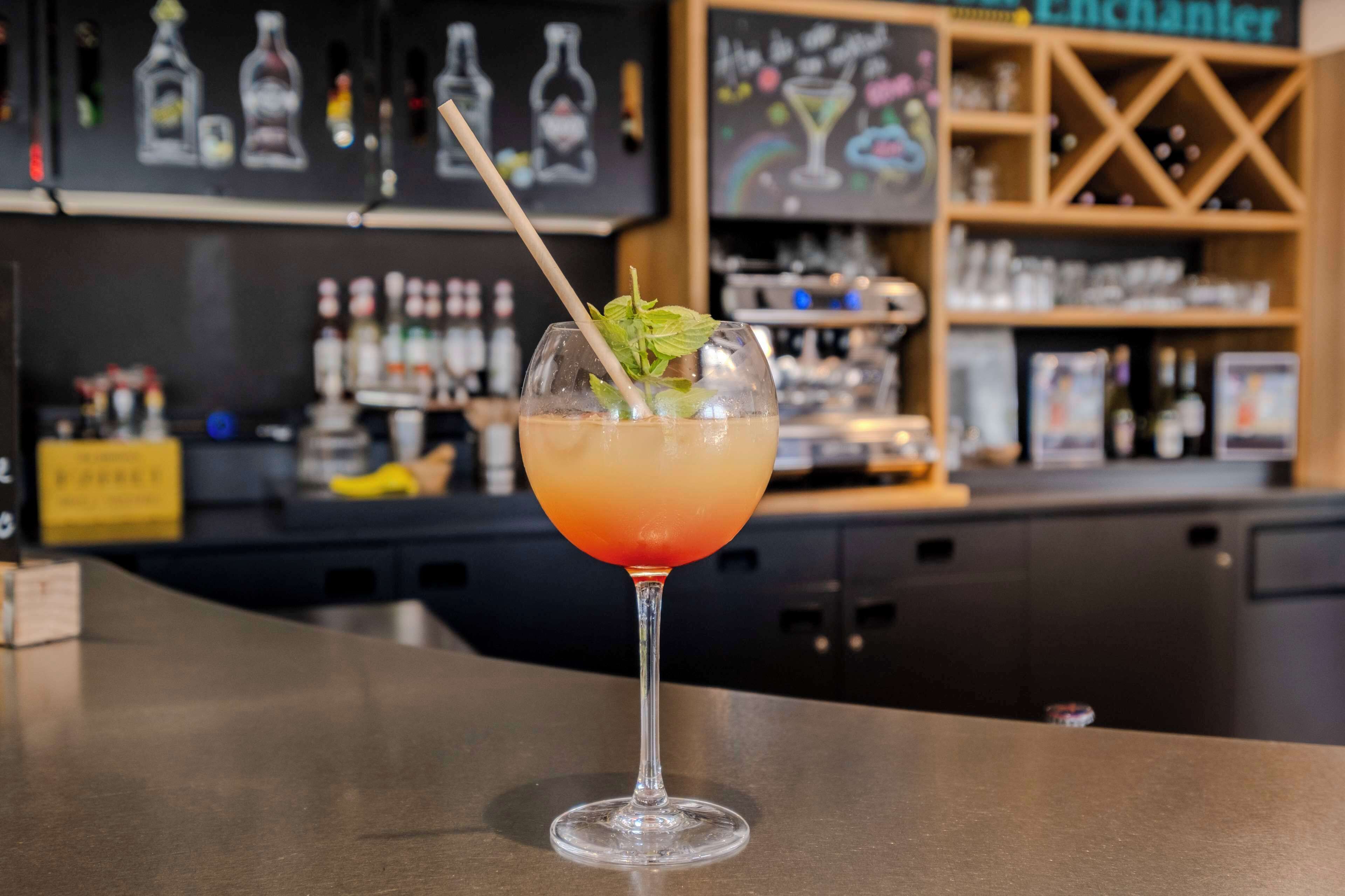 Eine Bar mit einem Cocktailglas auf der Theke, einer Speisekarte im Hintergrund und Regalen voller Flaschen.
