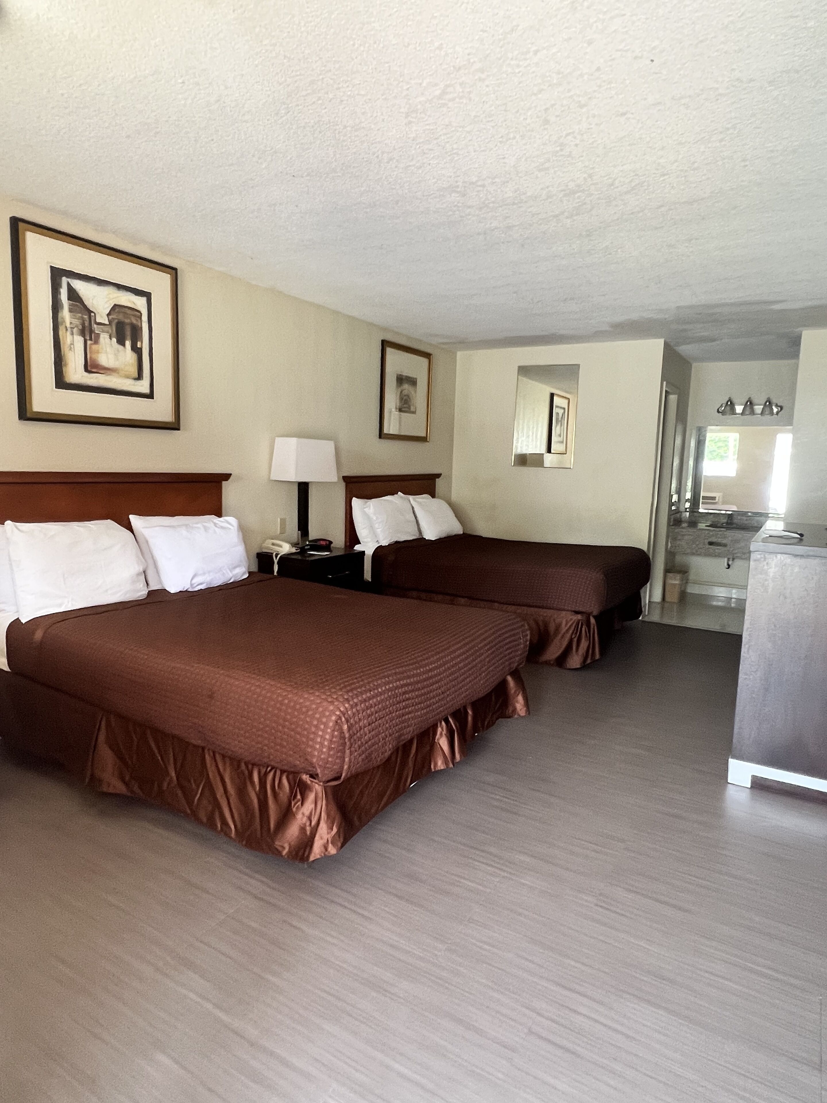 A hotel room with two beds, a desk, a lamp, and a mirror.