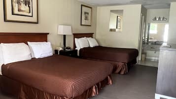 A hotel room with two beds, a desk, a lamp, and a mirror.