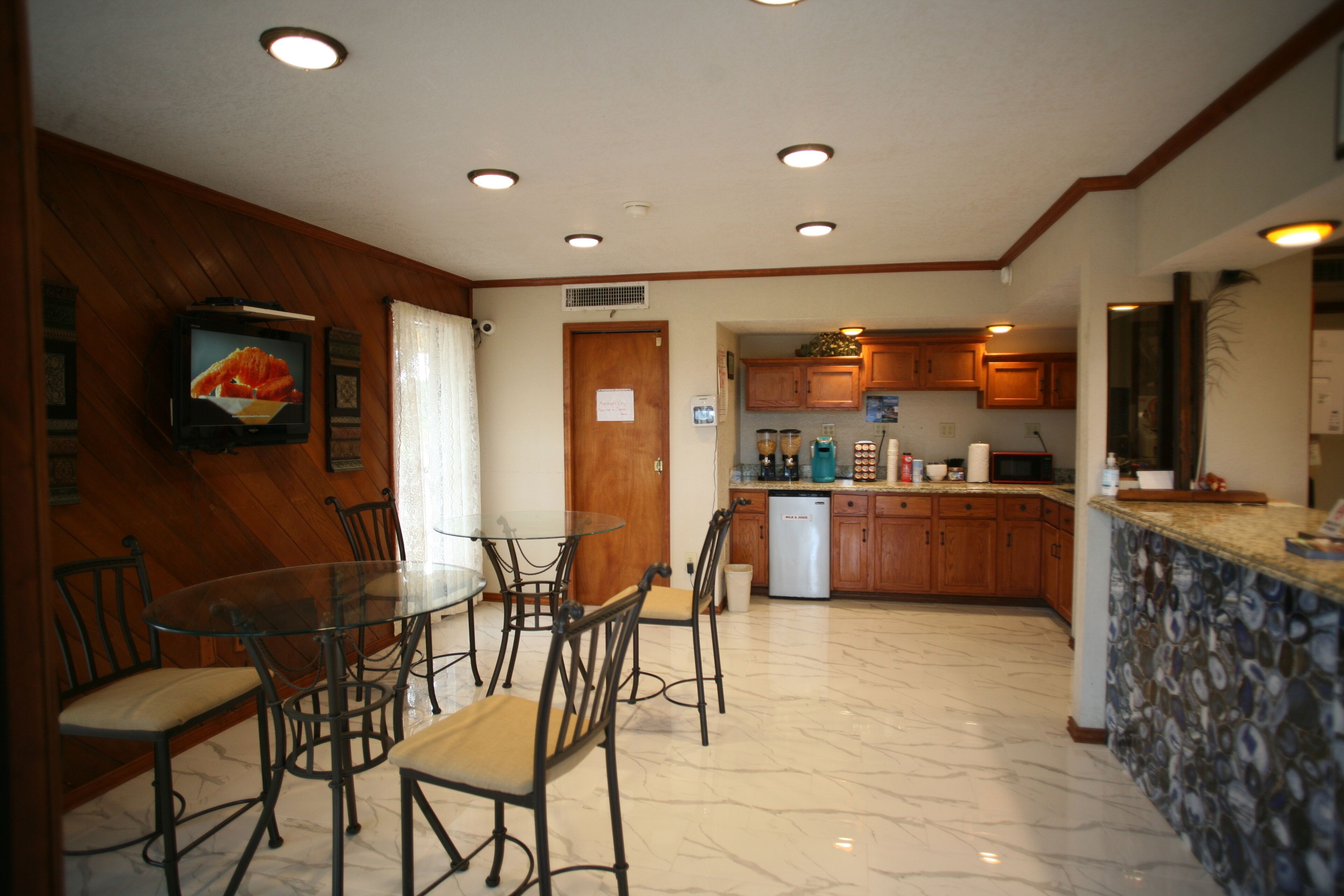 A dining area with a glass table and chairs, a kitchen with wooden cabinets, and a television on the wall.