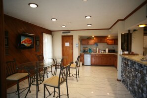 A dining area with a glass table and chairs, a kitchen with wooden cabinets, and a television on the wall.