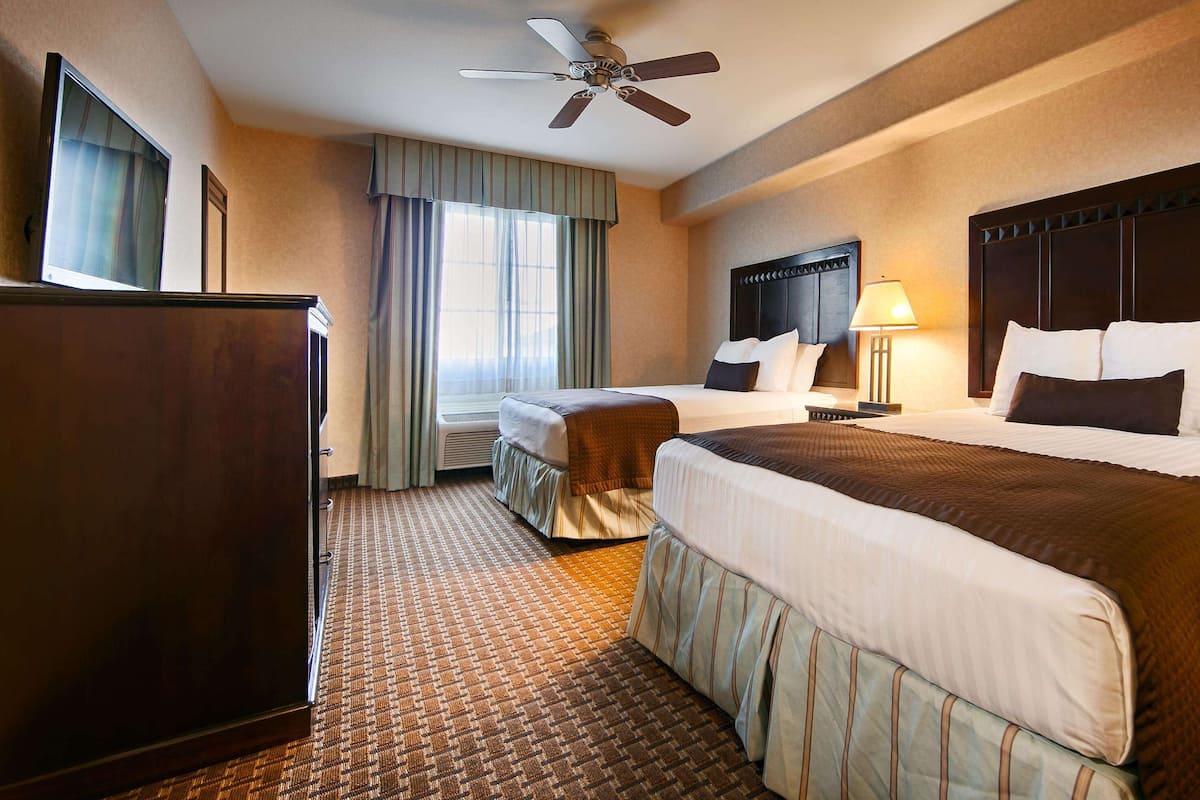 A hotel room with two beds, a ceiling fan, a desk, and a window with curtains.