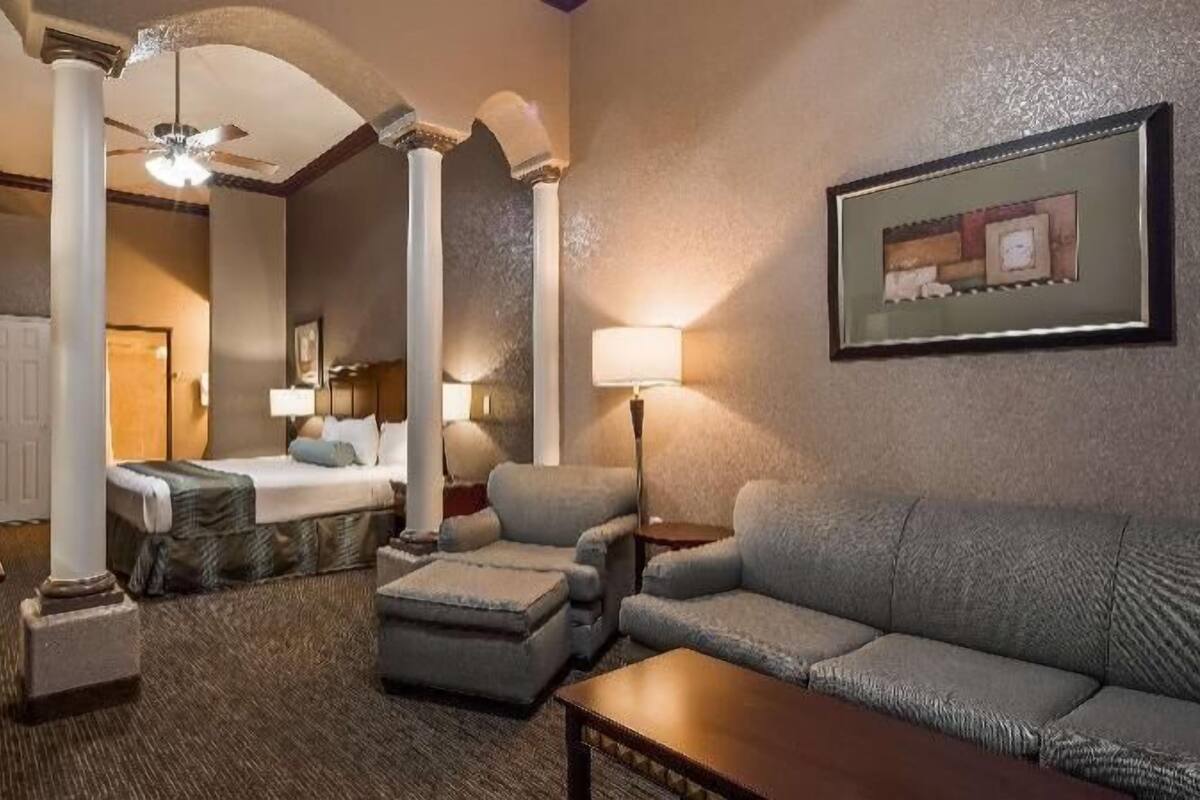 A hotel room with a bed, a sofa, a coffee table, a desk, and a ceiling fan.
