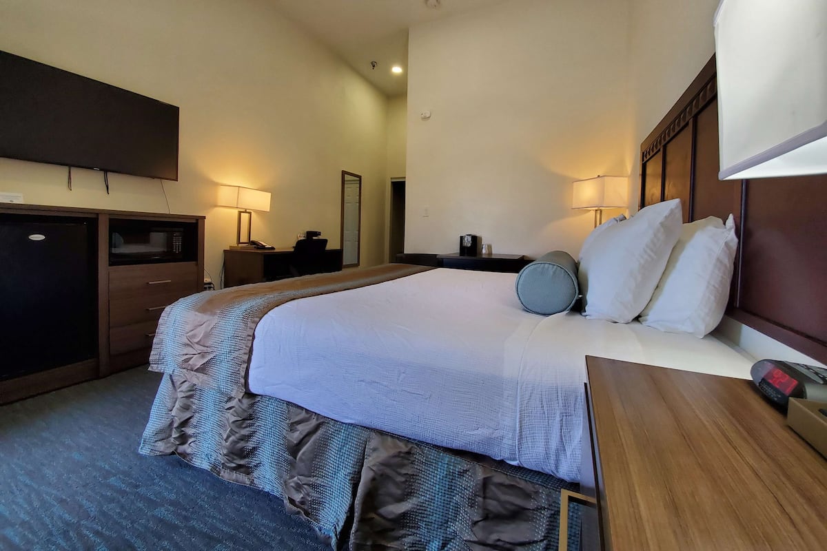 A hotel room with a large bed, bedside tables, a desk, a flat-screen TV, a mirror, and a wall-mounted lamp.