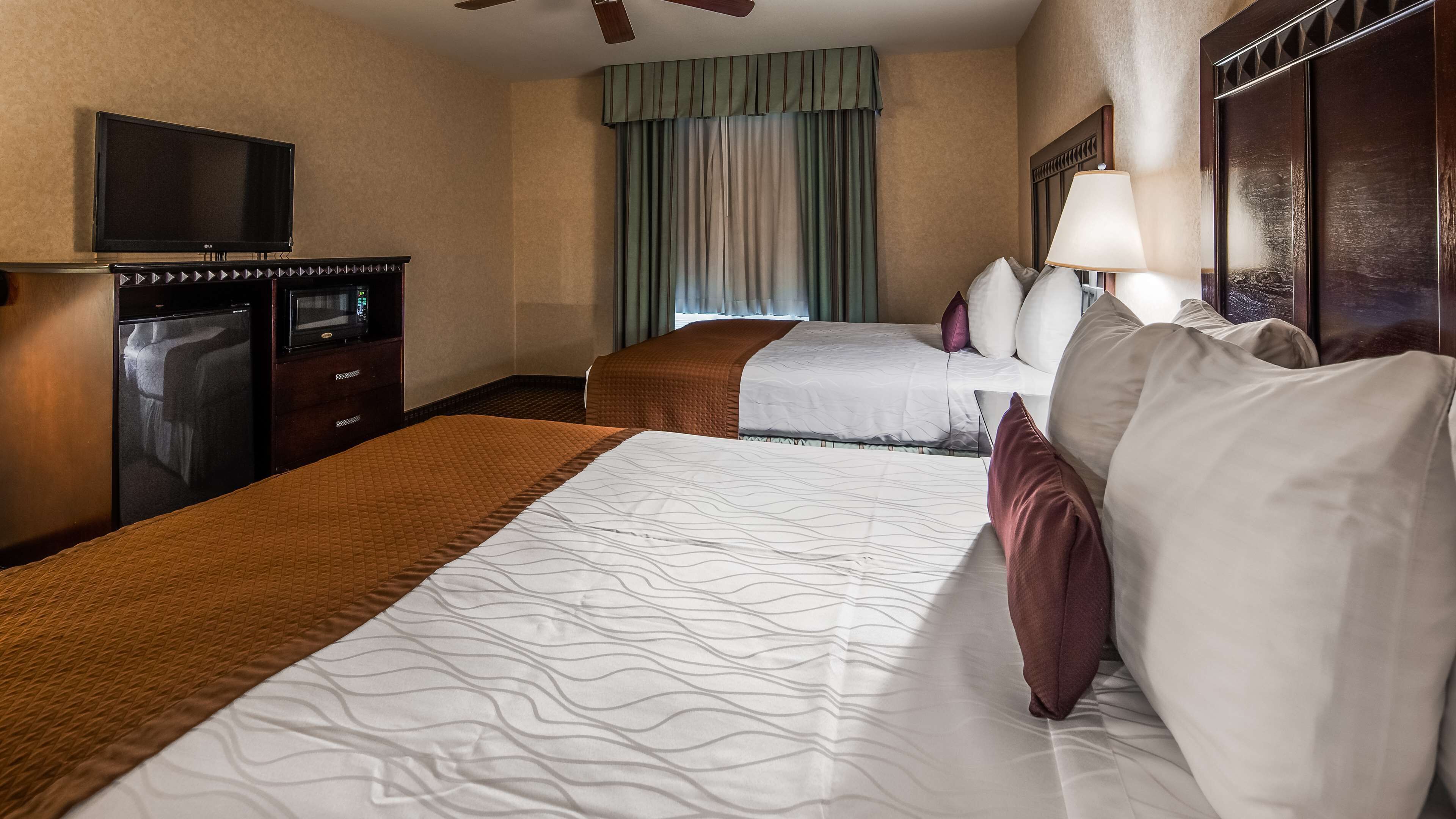 Een hotelkamer met twee bedden, een televisie, een minibar en een plafondventilator.