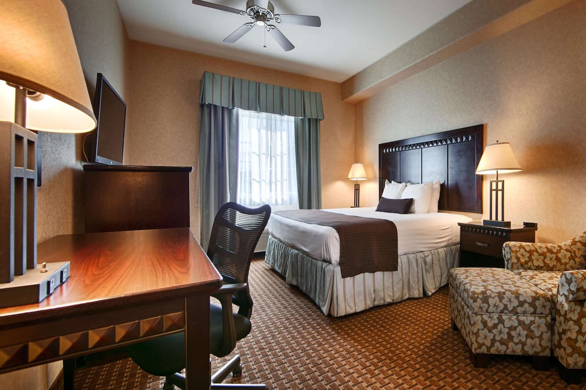 A hotel room with a bed, desk, chair, and TV.