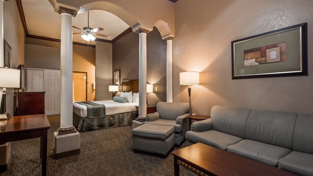 A hotel room with a bed, a sofa, a chair, a table, and a lamp. - Best Western Plus Main Street Inn (Brawley)