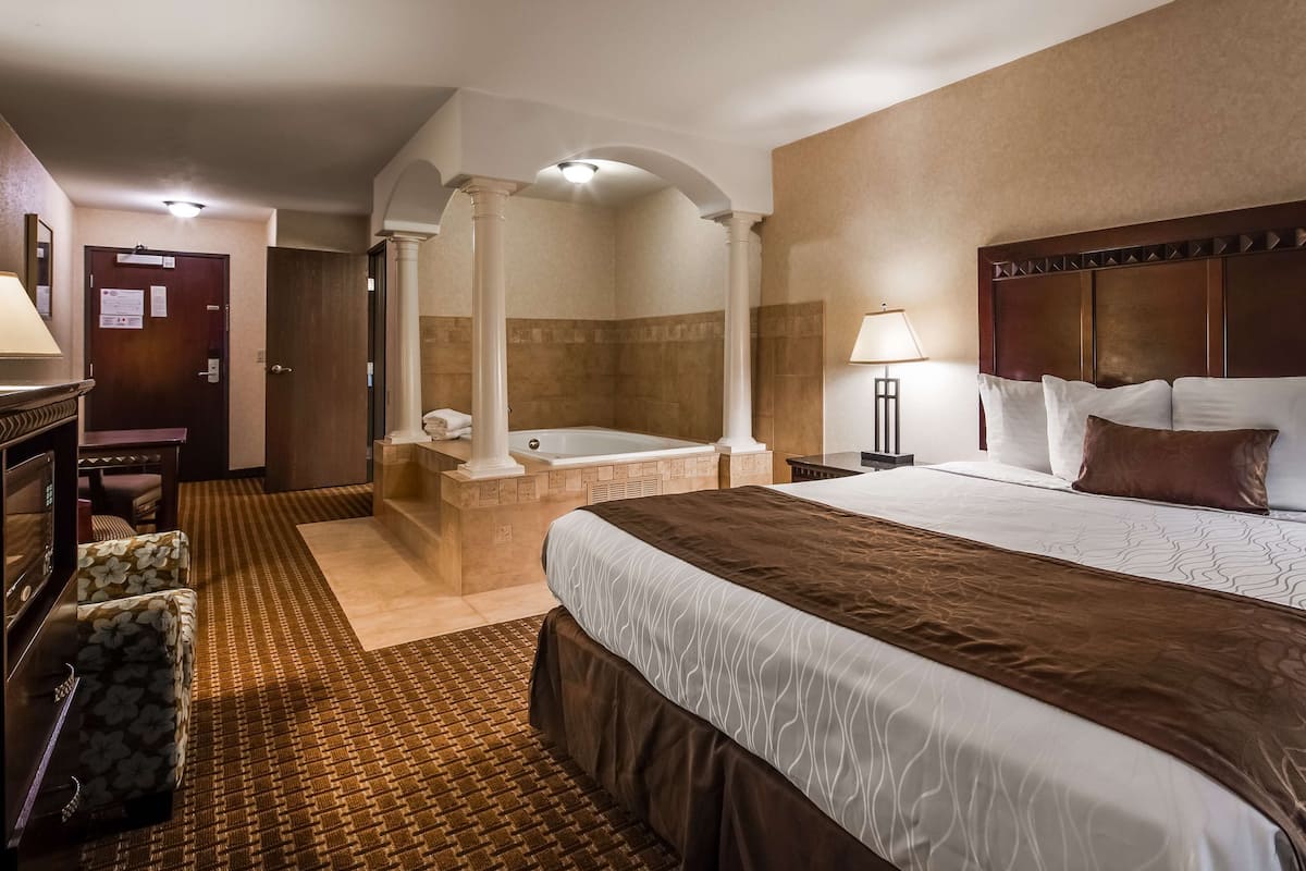A hotel room with a large bed, a separate bathroom with a bathtub, a desk, and a chair.