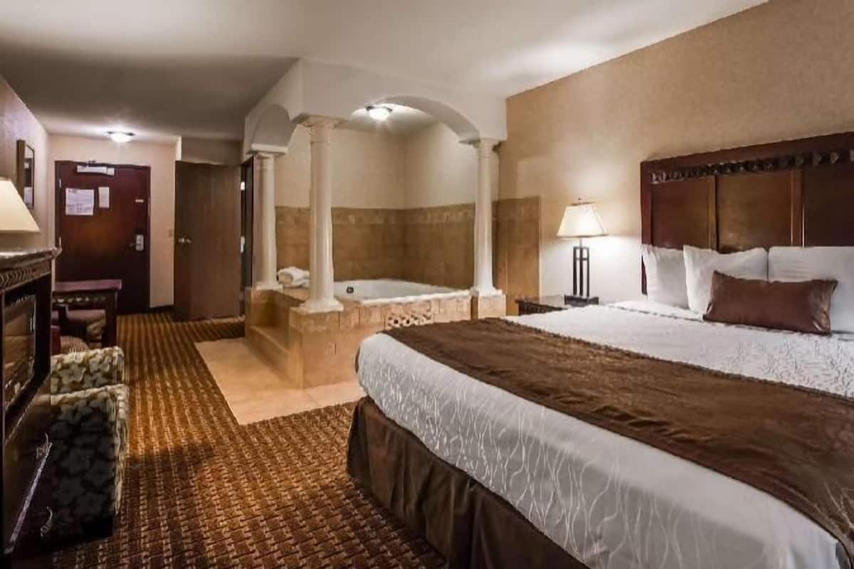 A hotel room with a large bed, a separate sitting area with a chair, a small table, a lamp, and a bathtub.