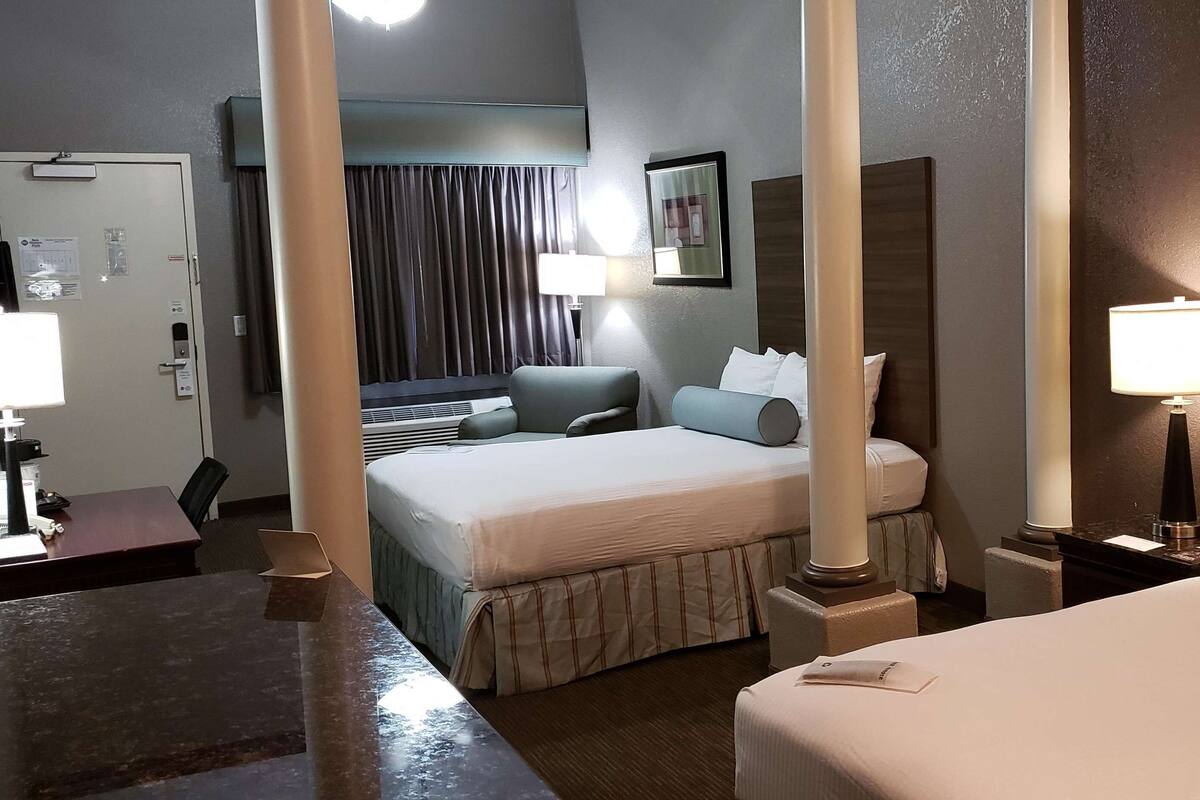 A hotel room with a bed, a desk, a chair, and a lamp.