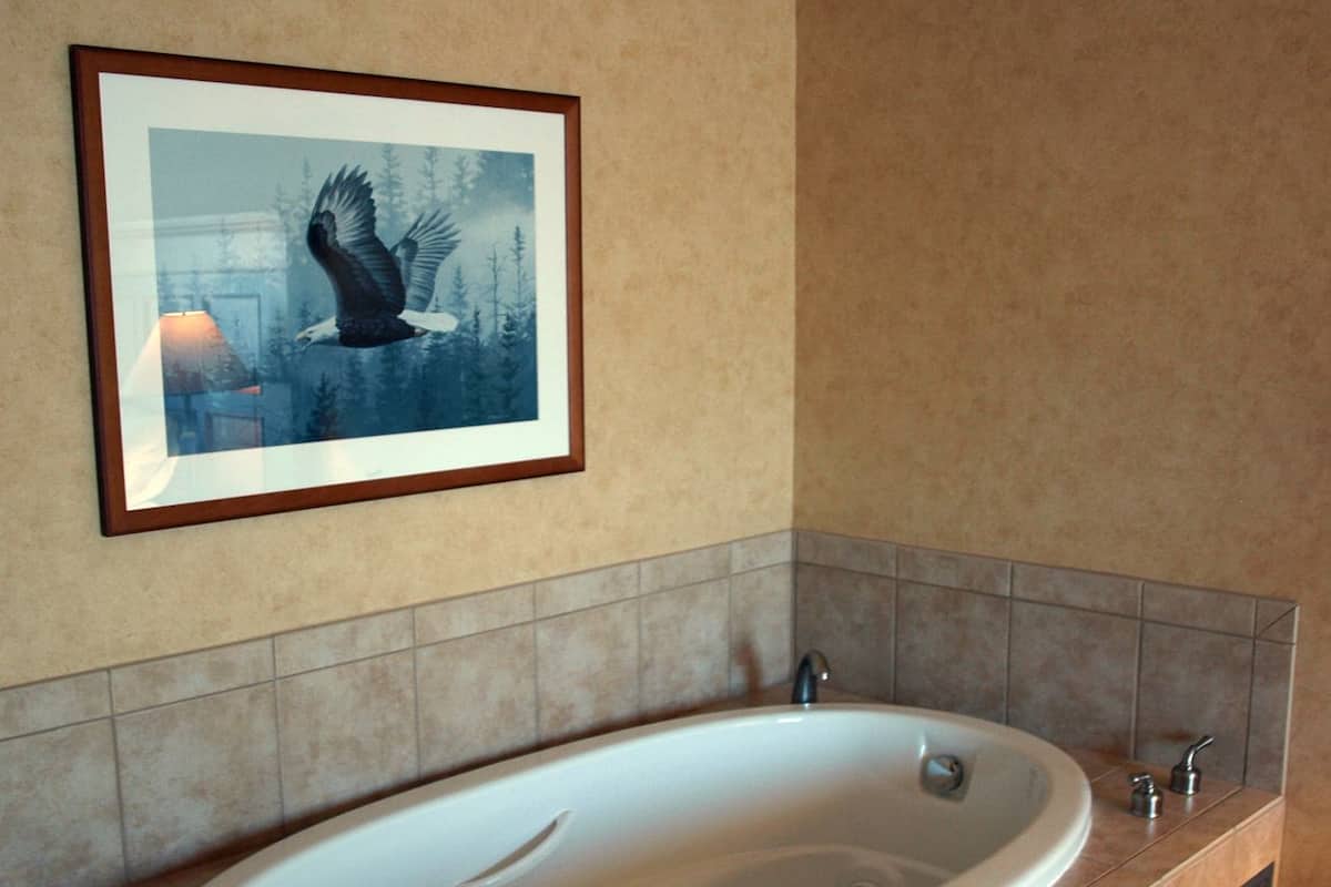 A modern bathroom with a freestanding bathtub, tiled walls, and a framed picture of an eagle.