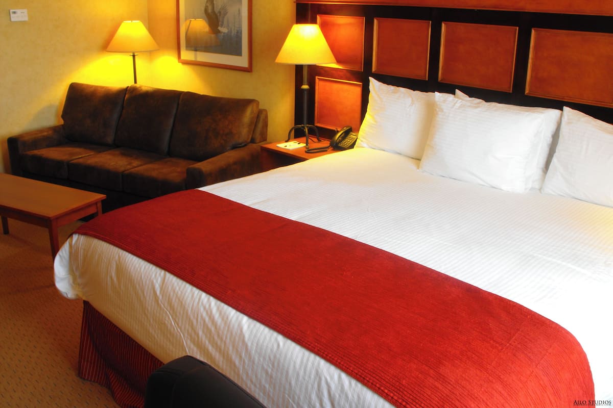 A hotel room with a large bed, a wooden headboard, a sofa, two bedside lamps, and a framed picture on the wall.