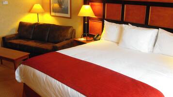 Quarto de hotel com uma cama grande, cabeceira de madeira, um sofá, duas luminárias de apoio e um quadro na parede.