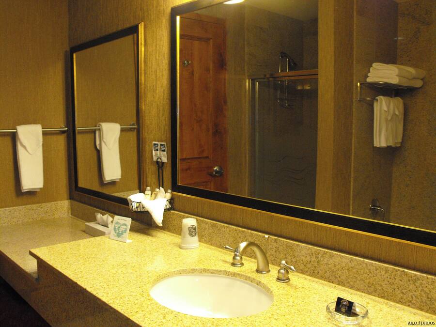 A hotel bathroom with a sink, mirror, towel rack, and a shower area.