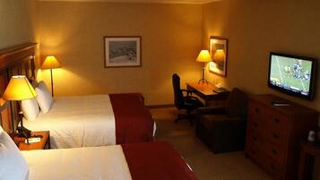 A hotel room with two beds, a desk, a chair, a television, and a dresser.