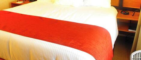 A hotel room with a large bed, a wooden headboard, a telephone, and a lamp on a nightstand.