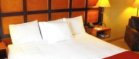 A hotel room with a large bed, a wooden headboard, a bedside table with a lamp, and a chair.