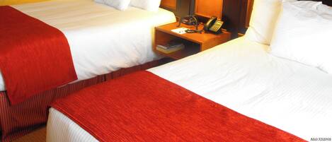 Una habitación de hotel con dos camas, una mesita de noche, un teléfono y una lámpara.