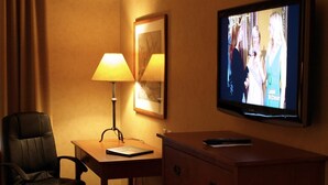 Una habitación de hotel con escritorio, una silla, lámpara, televisor y cómoda.