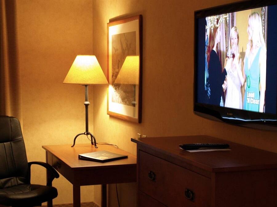 A hotel room with a desk, a chair, a lamp, a television, and a dresser.