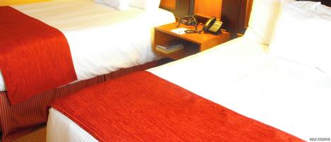 A hotel room with two beds, a desk with a telephone, and two lamps.