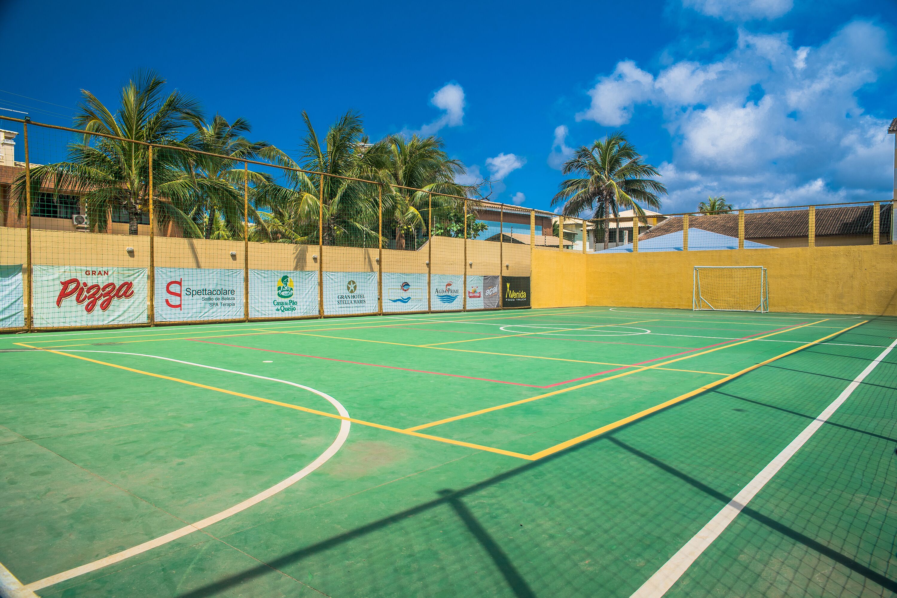 An indoor sports court with a green surface, surrounded by a fence, and advertising banners.