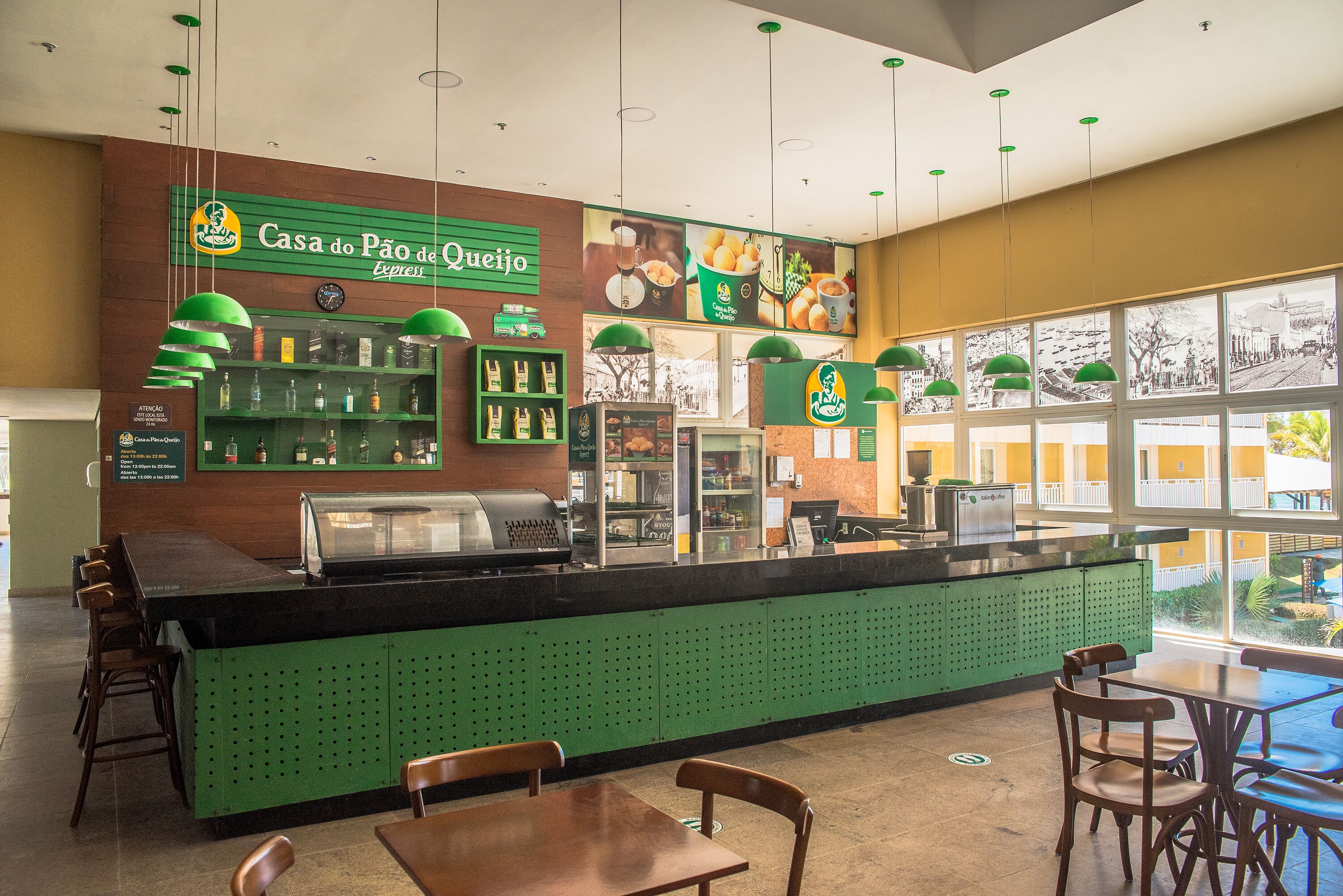 Un café con mostrador verde, sillas de madera y vistas amplias a través de grandes ventanales.