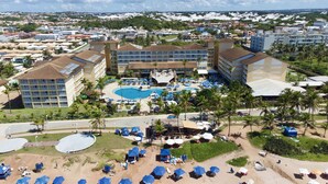 Un complexe hôtelier comprenant plusieurs bâtiments, une piscine centrale et de nombreux parasols de plage.
