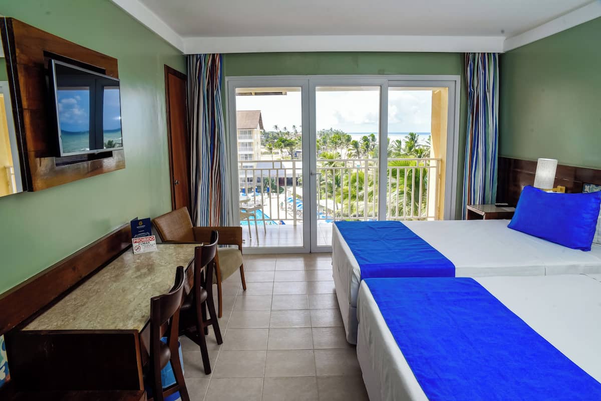 Ein Hotelzimmer mit Balkon, einem Bett, einem Schreibtisch und einem Fernseher.