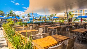 Un espace extérieur aménagé pour les repas, avec des meubles en osier et des parasols, offrant une vue sur une piscine et des palmiers.