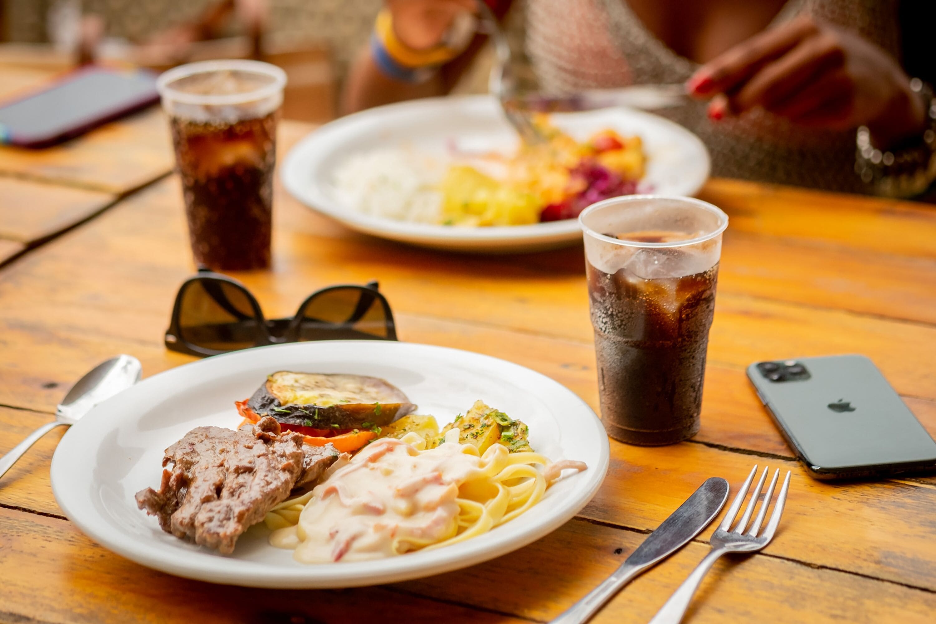 A wooden table with a plate of food, a drink, and a smartphone.