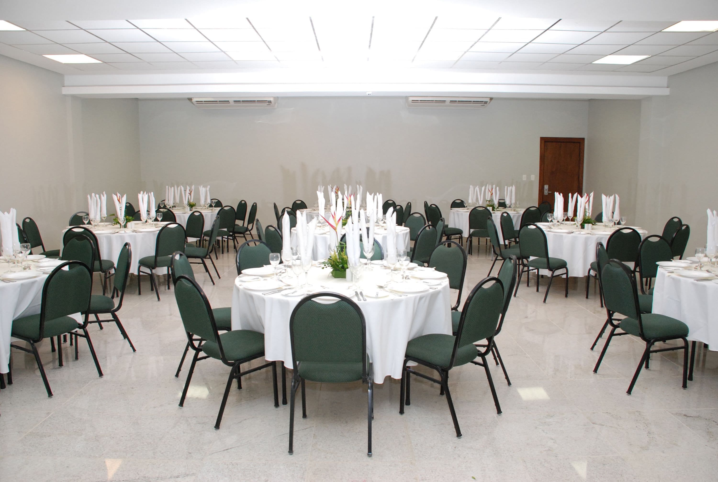 A large conference room with round tables, green chairs, and white tablecloths.