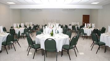 A large conference room with round tables, green chairs, and white tablecloths.