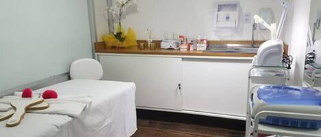 A clinical room with a bed, a medical cart, and a sink.