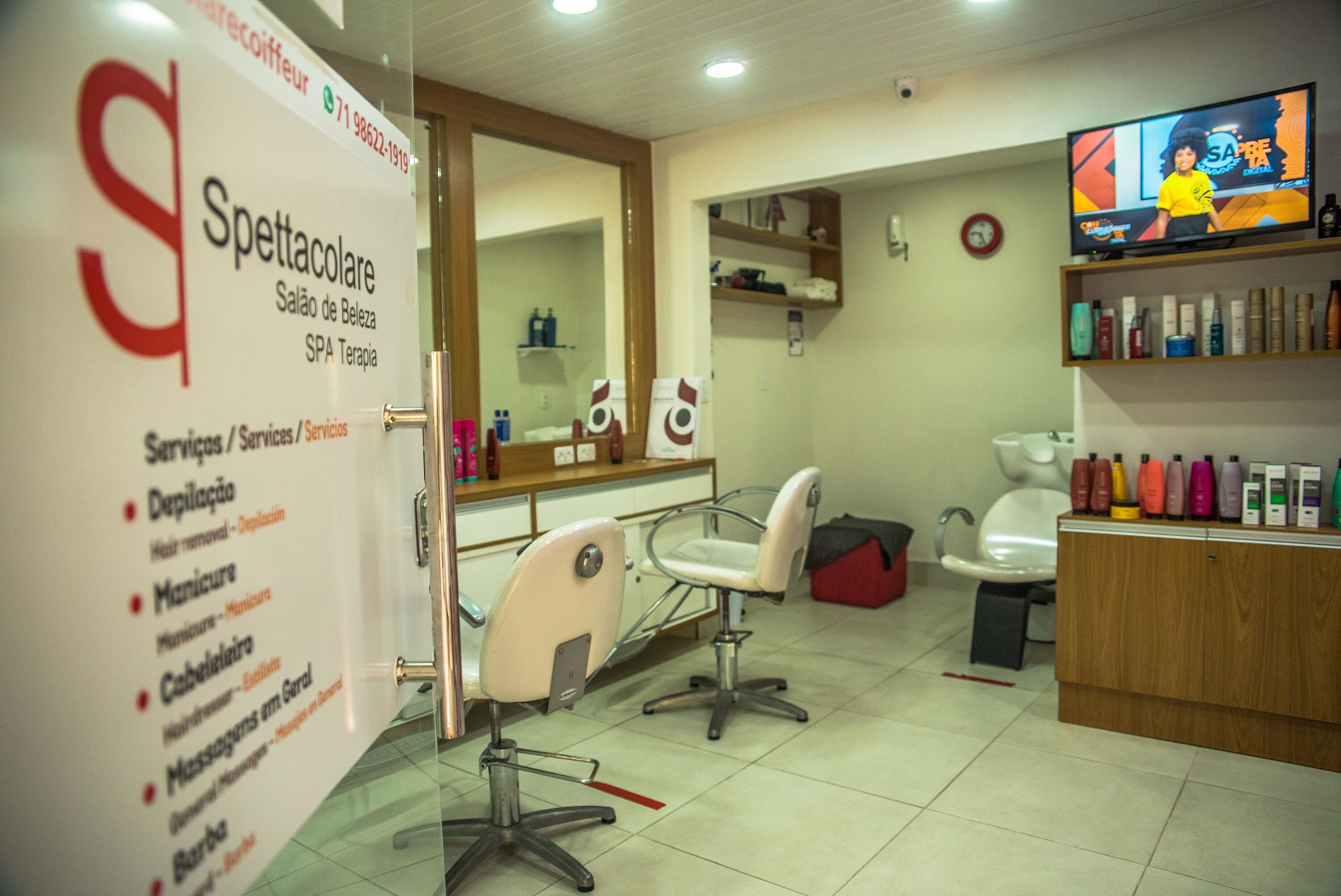 A salon interior with two chairs, a mirror, shelves with products, and a TV displaying a program.