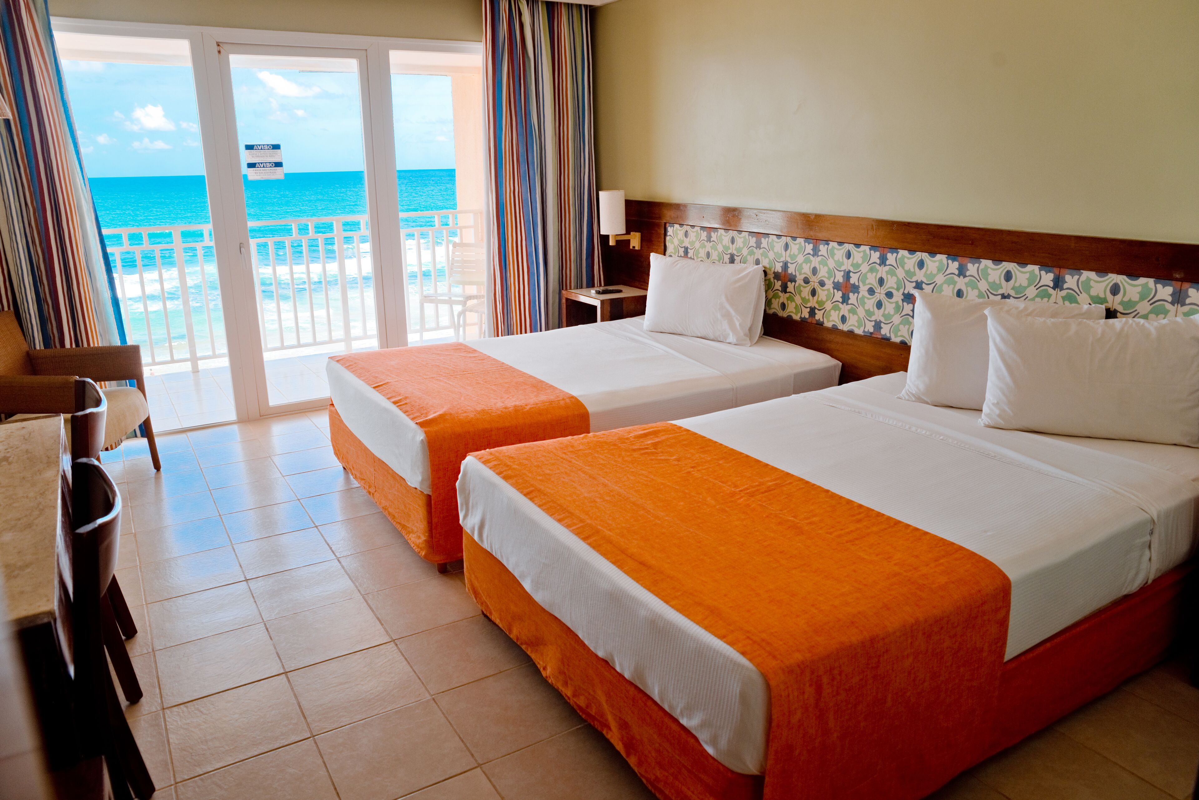 A hotel room with two beds, a balcony with a view of the ocean, and a dining area with a table and chairs.