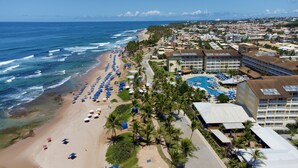 Une station balnéaire dotée d’une longue plage, d’un espace piscine central et de plusieurs bâtiments d’hôtel.