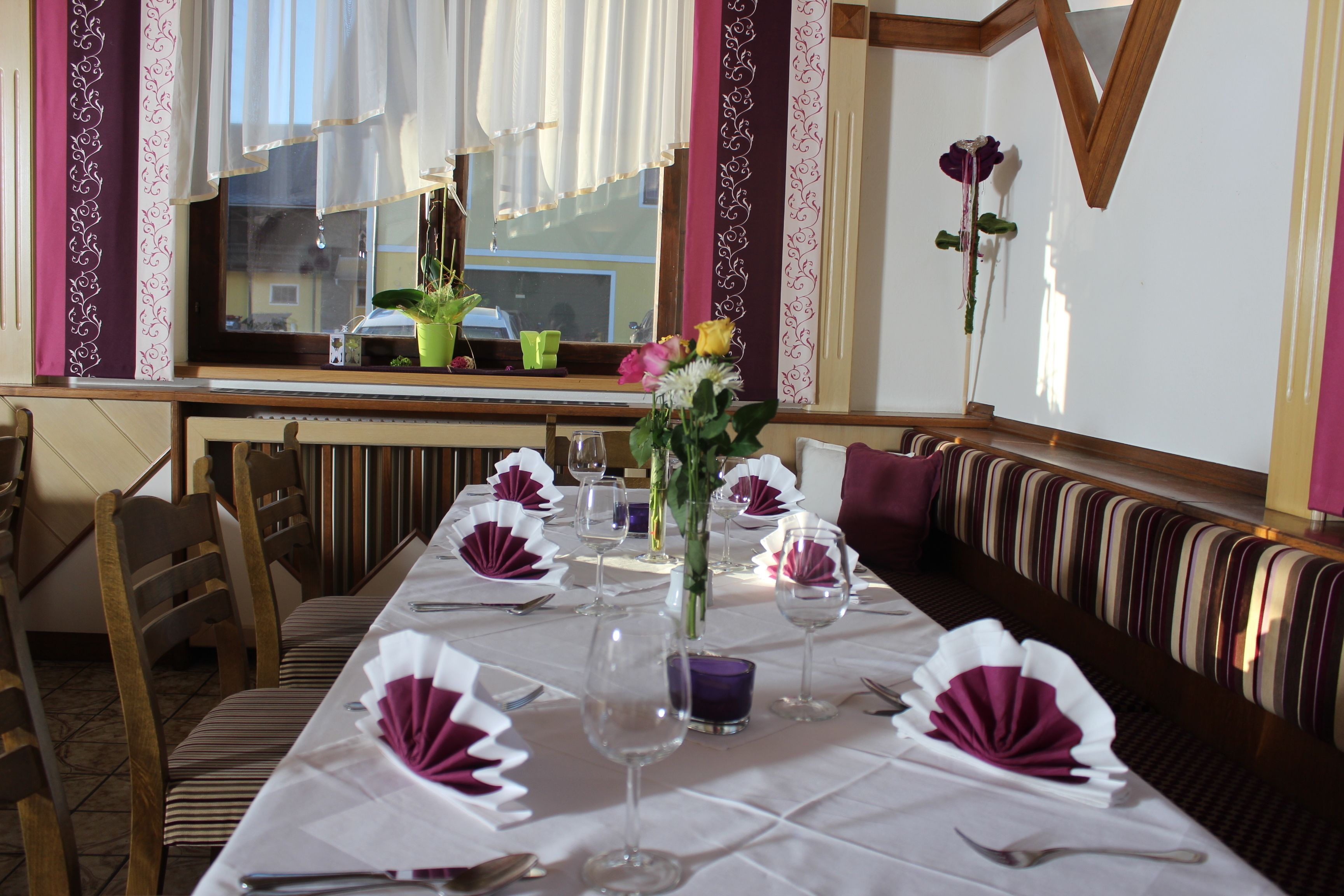 A dining area with a long table set for a meal, chairs, a bench, and a window with curtains.