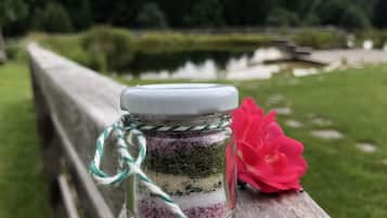 Un bocal de vidre amb tapa blanca, amb materials en capes, col·locat sobre una superfície de fusta amb una flor rosa a prop.
