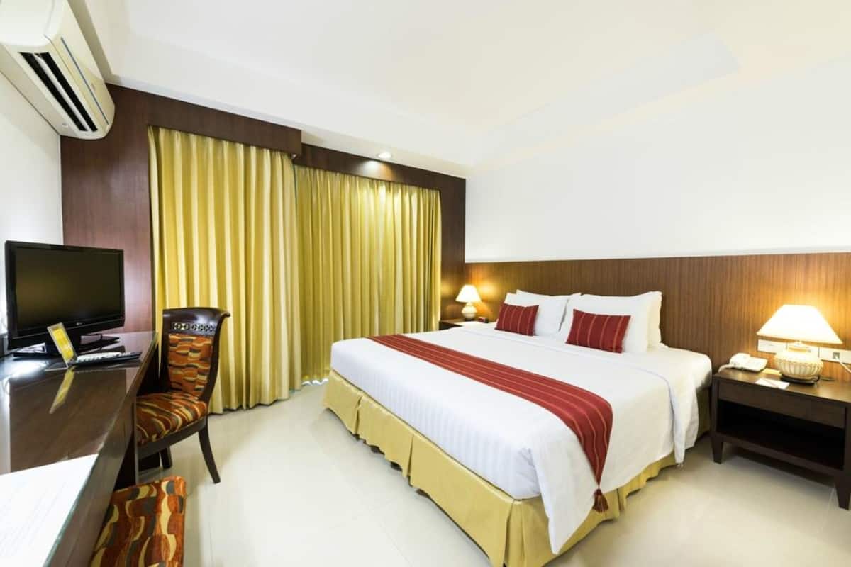 A hotel room with a bed, a desk with a computer, a chair, a TV, and a lamp.