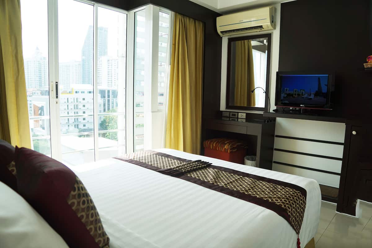 A hotel room with a large bed, a television, a mirror, and a view of the city through the window.