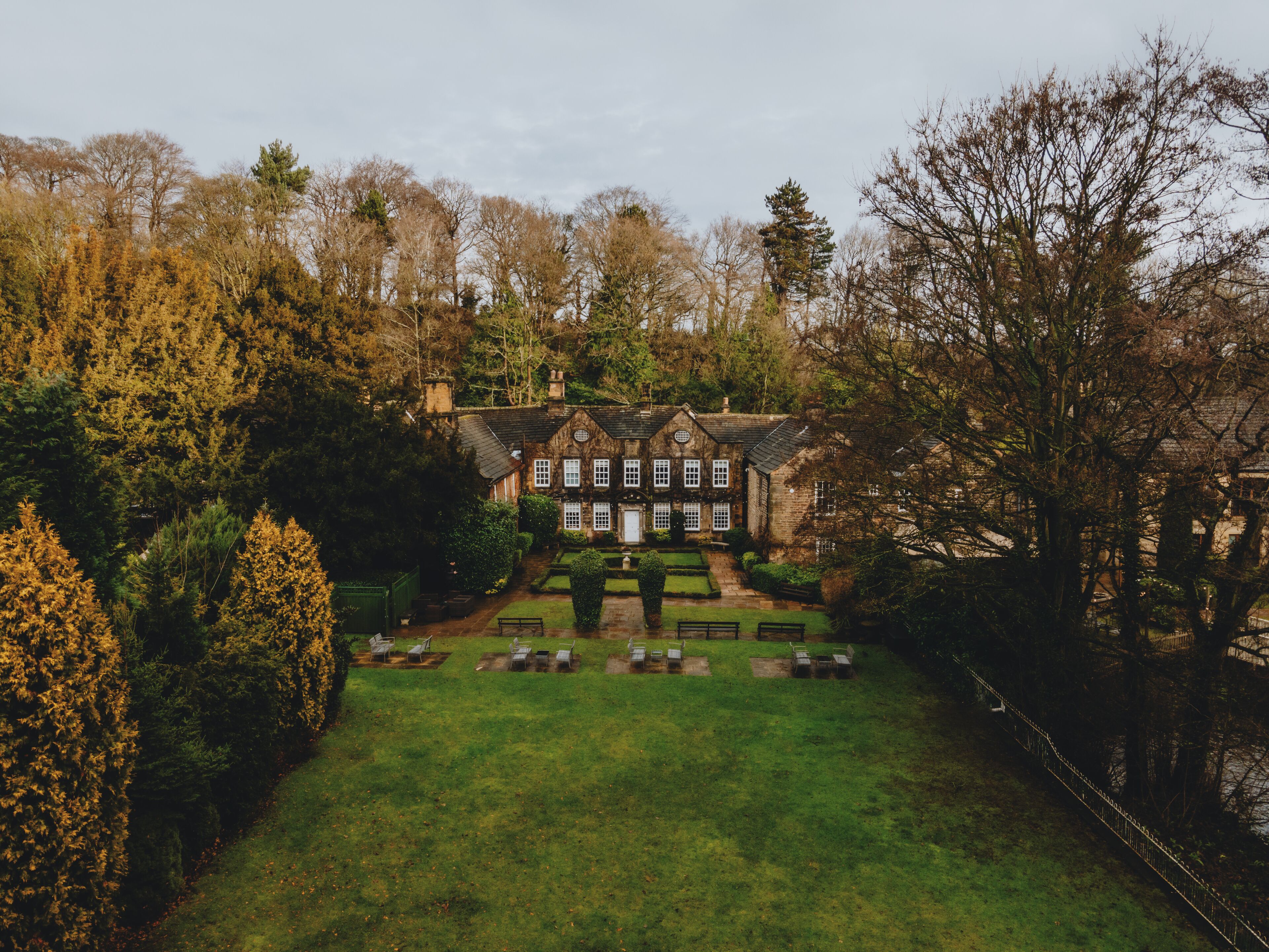Une grande maison traditionnelle en pierre, dotée d’une façade symétrique, entourée d’un jardin bien entretenu et d’un petit étang.