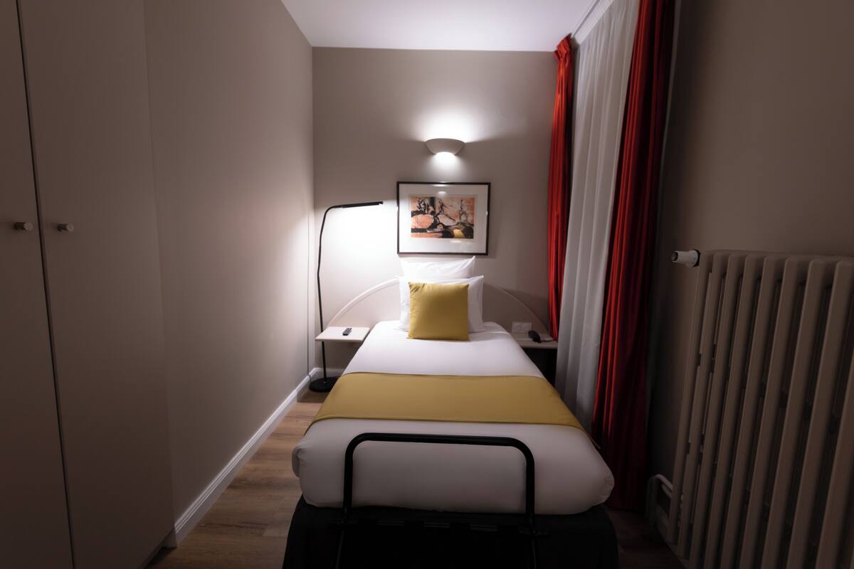 Un dormitorio pequeño y ordenado con cama, mesita de noche, lámpara y un cuadro enmarcado en la pared.