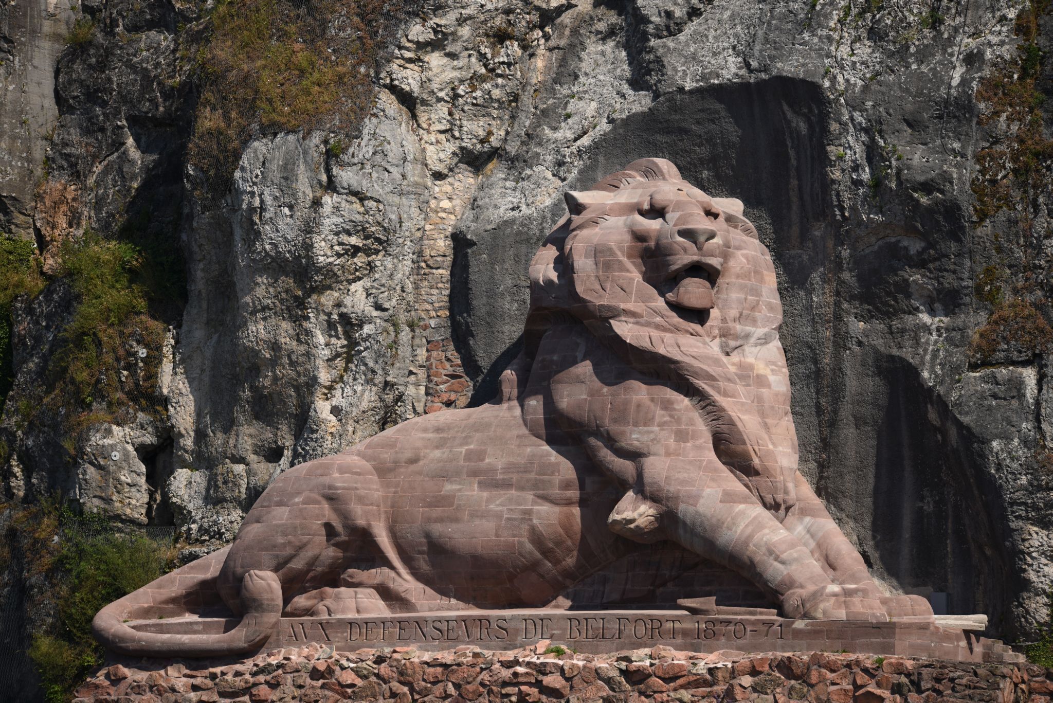 A lion statue with inscriptions on a rocky cliff.