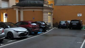 Un estacionamiento con varios coches aparcados frente a un edificio de fachada amarilla y estilo arquitectónico clásico.
