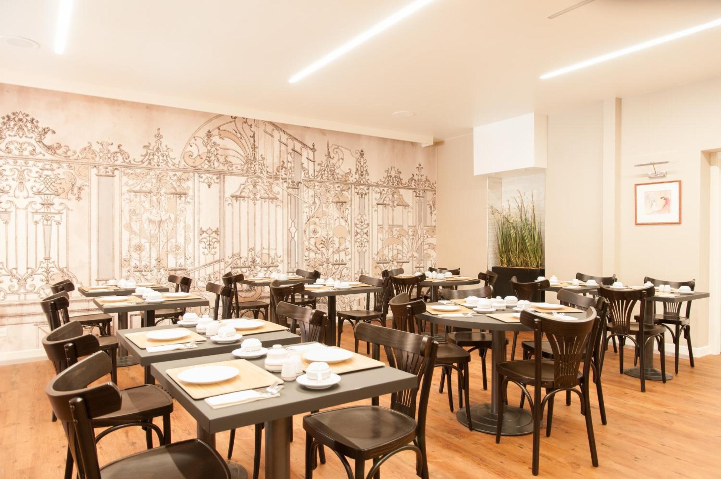 Un restaurante con mesas dispuestas para comer, que presenta una pared decorativa y una planta en maceta.