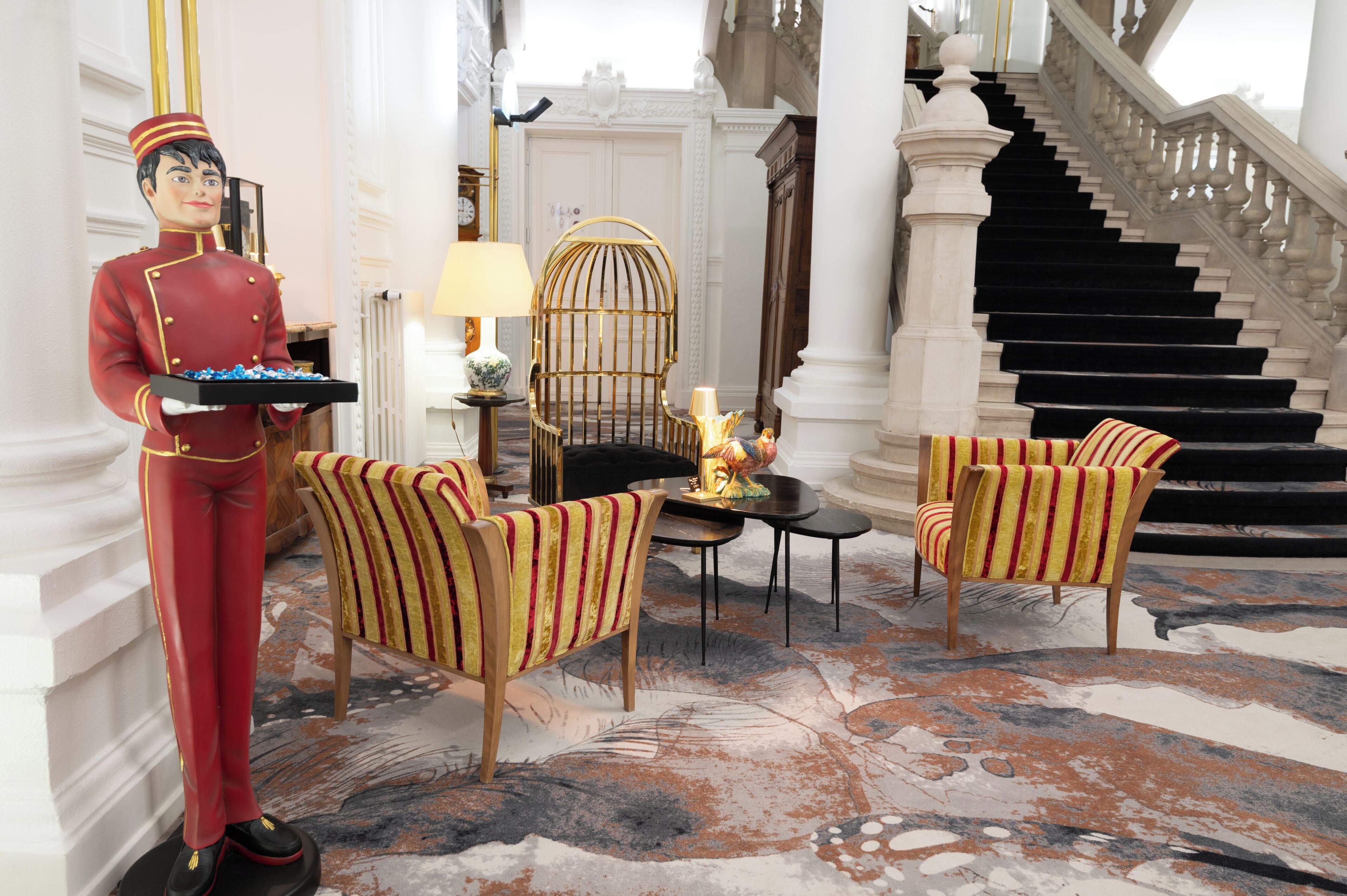 A statuary figure, a striped armchair, a round table with a lamp, and a staircase.