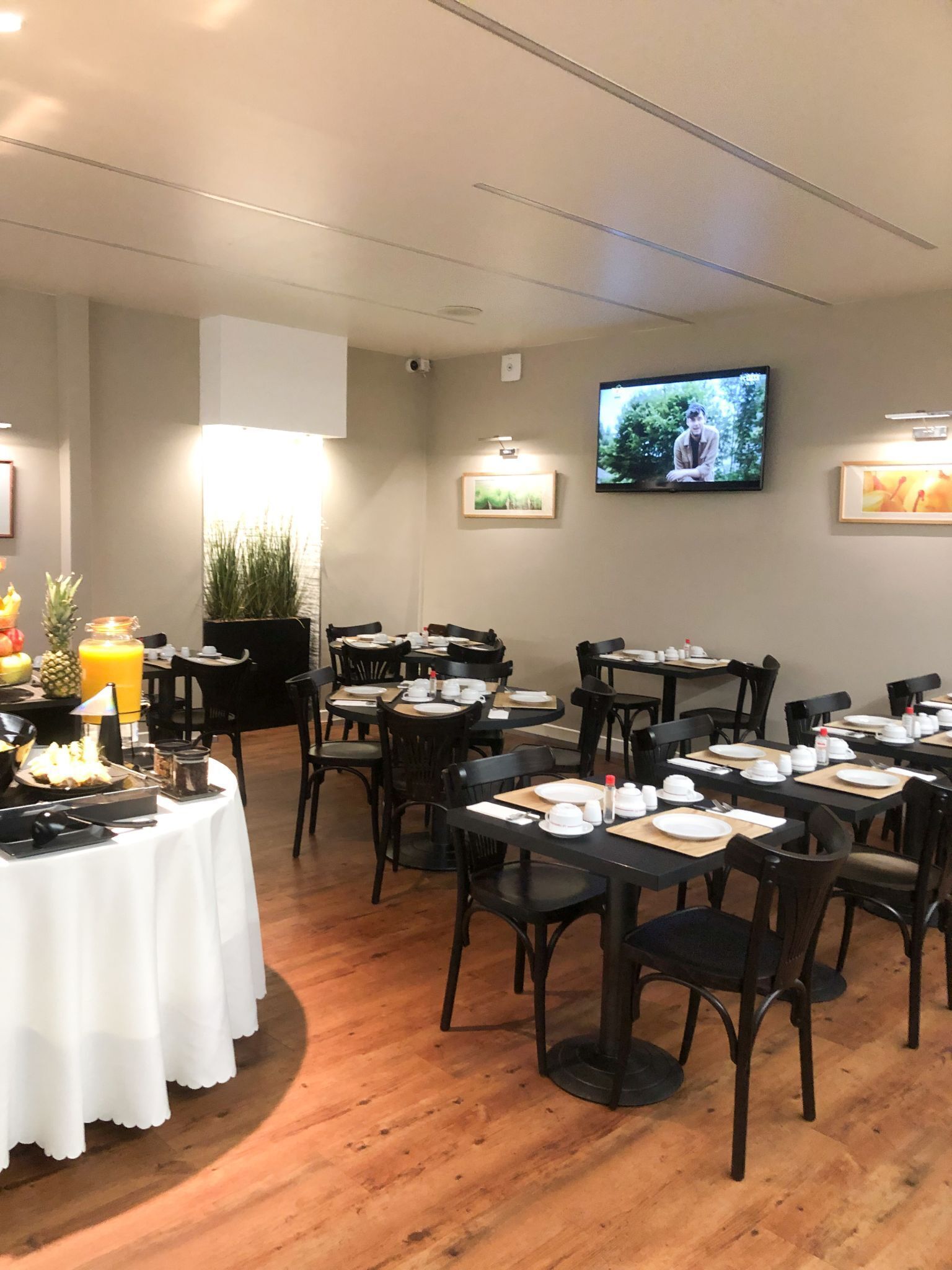A dining area with tables set for a meal, a television mounted on the wall, and a plant in the corner.